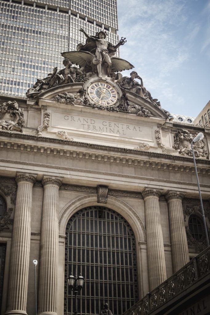 From below of aged stone Grand central terminal with sculpture and clock on top of roof located in New York city in Manhattan
